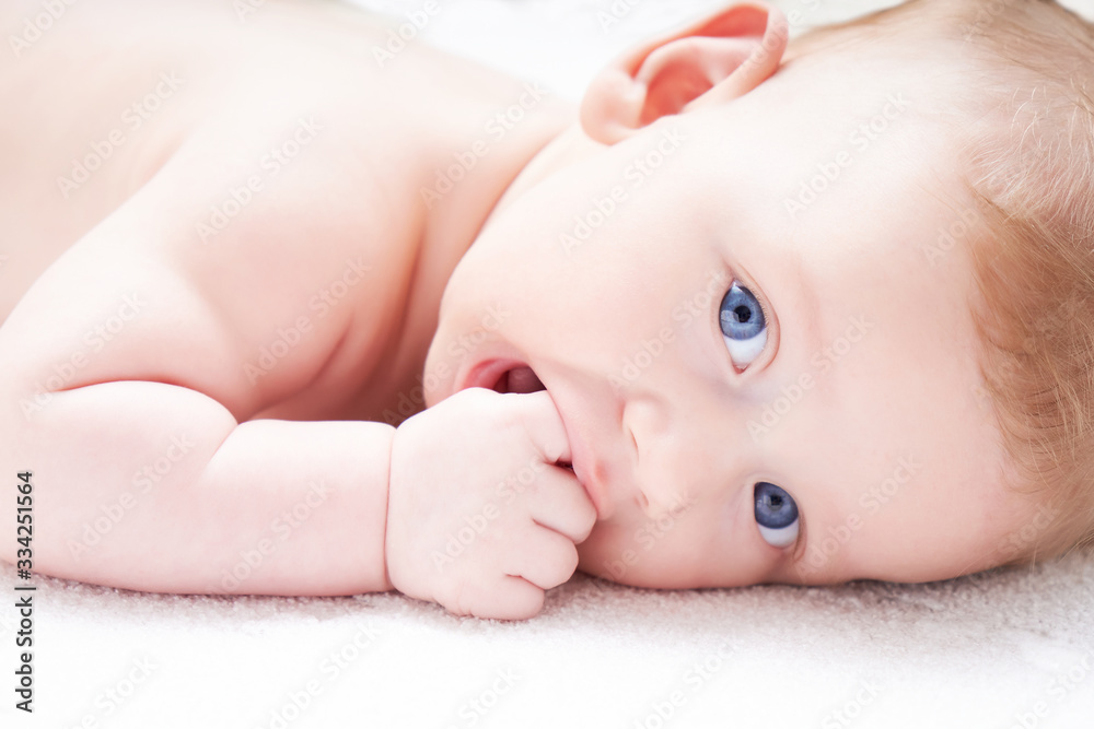 Cute baby with blue eyes sucks fingers, fist. On a light background Close up Cute baby with blue eyes sucks fingers, fist. On a light background Close up