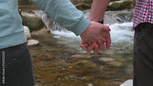 Close-up of a man and a woman holding hands near a mountain river, a mountain stream in the background.