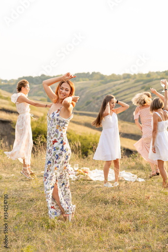The company of happy female friends having fun and dancing outside in a picnic at hills.