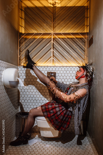 a punk girl sitting on the toilet straightens her torn black stockings. The girl has a stocking mask on her head
