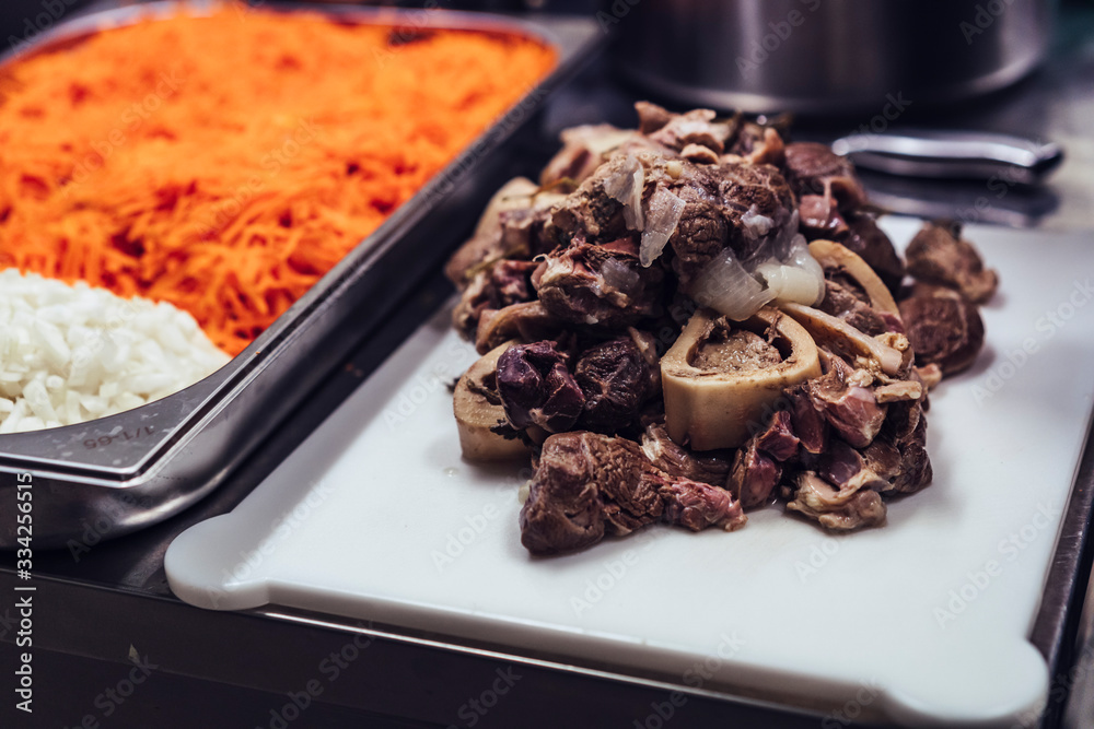 Boiled meat pieces with bones on white plastic cutting board, restaurant meal prepare Boiled meat pieces with bones on white plastic cutting board, restaurant meal prepare