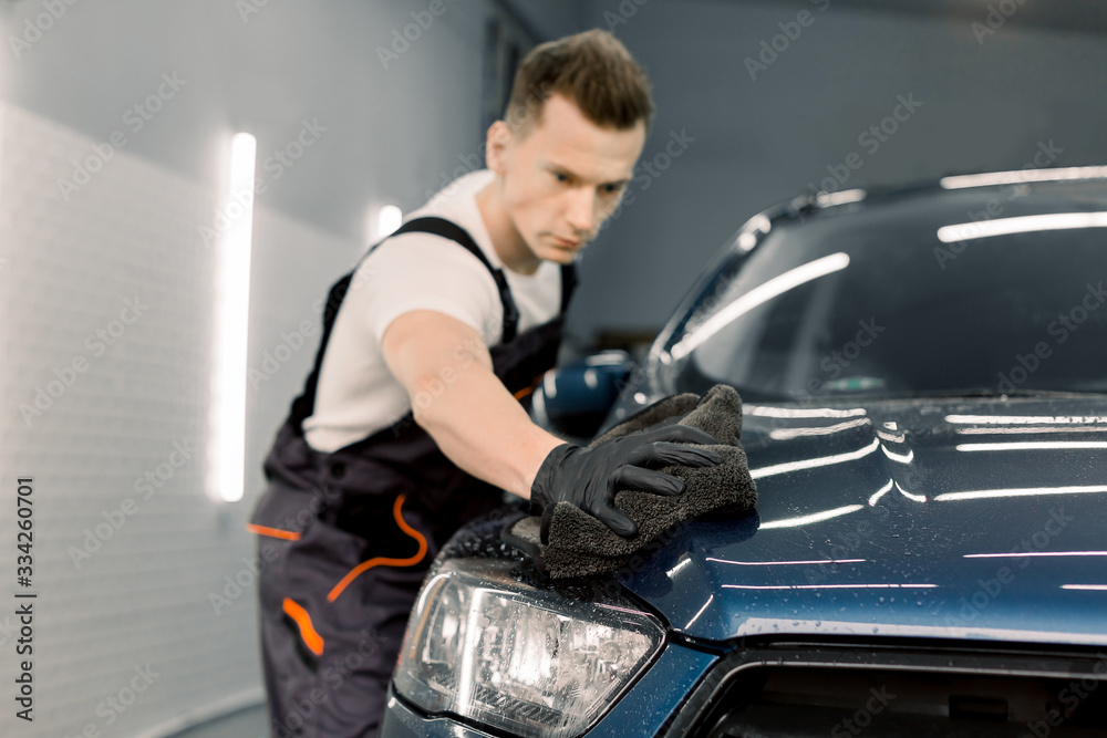 Car detailing and cleaning concept. Male car wash worker holds the microfiber in hand and polishes the car hood. Selective focus on the hand with microfiber. Car detailing and cleaning concept. Male car wash worker holds the microfiber in hand and polishes the car hood. Selective focus on the hand with microfiber.