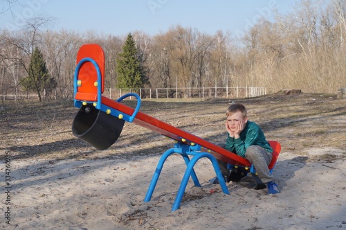 A overweight boy sits on a swing and is bored. The concept of childhood depression, difficult age, childhood has passed, empty playgrounds.