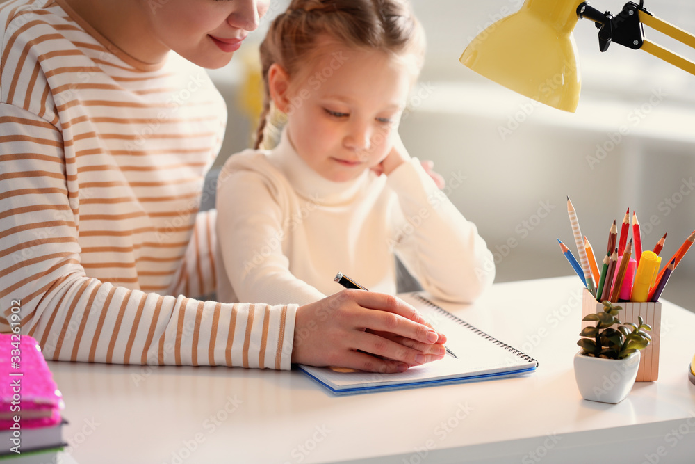 Woman helping her daughter with homework at table indoors Woman helping her daughter with homework at table indoors