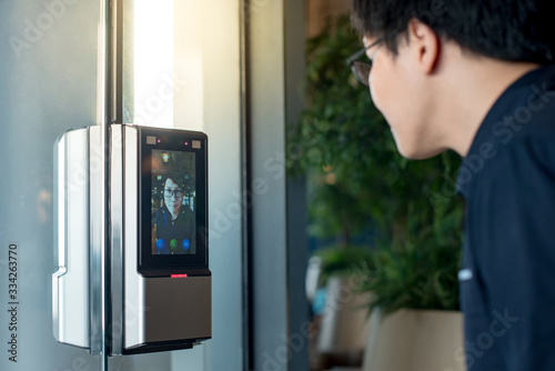 Authentication by facial recognition concept. Biometric admittance control device for security system. Asian man using face scanner to unlock glass door in office building. photo