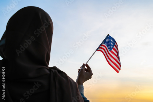 Silhouette of muslim woman in scarf with American, flag of at sunset. America. Concept