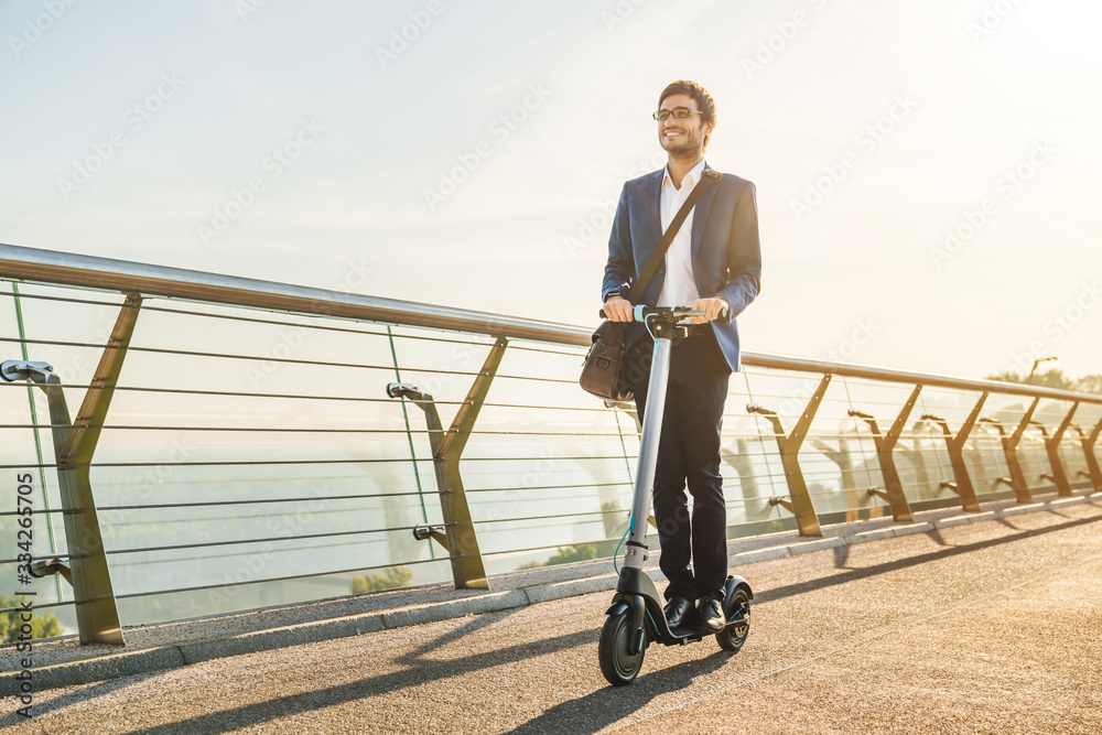 Ecological transportation concept. Young business man in suit riding electric scooter in office