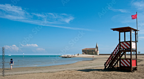 Girl on the beach of Caorle, a beautiful seaside resort in the Veneto, in the background the church of Madonna dell'Angelo. Italy