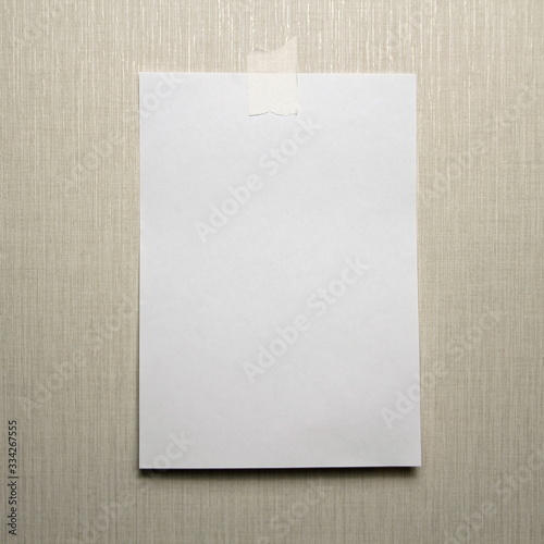 A4 white sheet of paper hanging on a wall glued with a piece of paper tape on a light background.