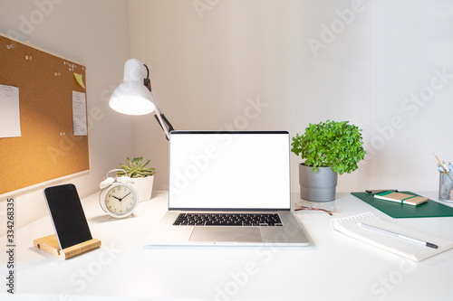 Laptop with blank white screen on office desk interior. Stylish rose gold workplace mockup table view.