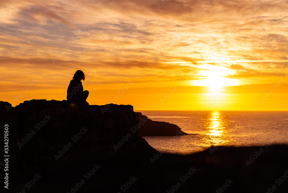 Silhouette of young woman on the edge of the cliff with sea view during sunrise. Holidays and enjoying life concept