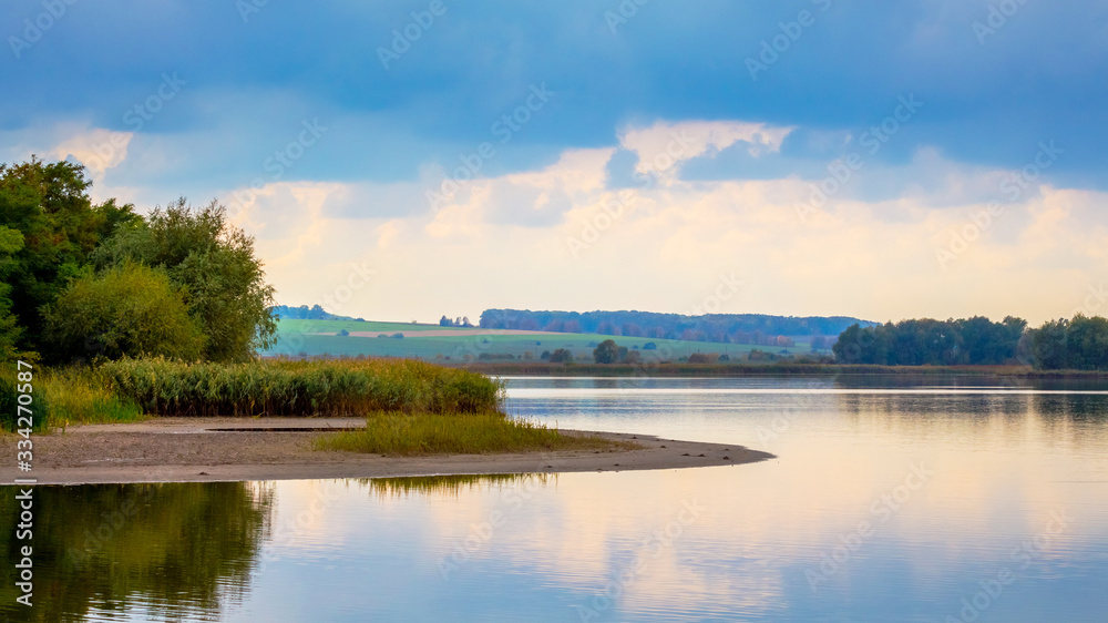 Summer landscape with river, trees and clouds reflecting in the water
