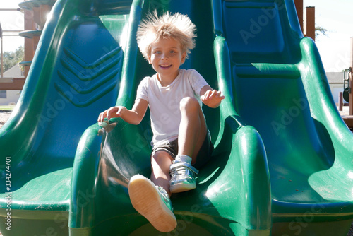 Smiling boy going down a slide with hair sticking up due to static electricity photo