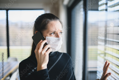 Worried woman with telephone and face masks indoors at home, Corona virus concept.