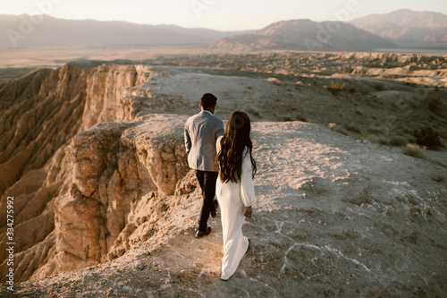 man and woman holding hands and walking along a cliff together