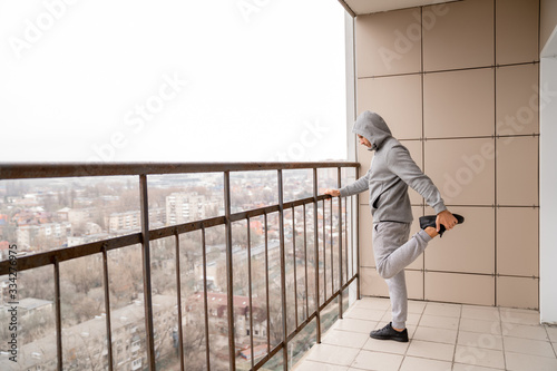 Self-isolation and quarantine concept. A man in sportswear plays sports on the balcony of his house.