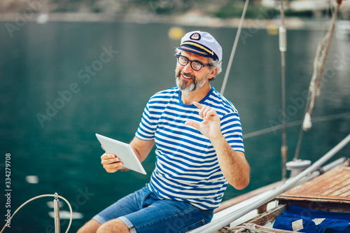 Mature man standing on the deck of his boat and using digital tablet on a sunny afternoon.