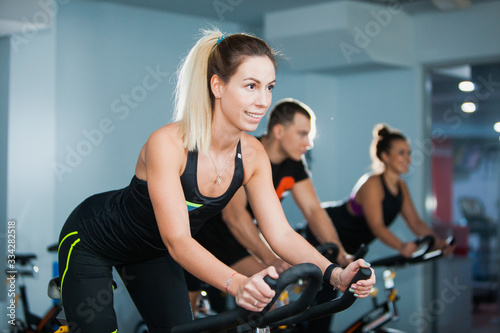 Cycling class in fitness club, group of fit people spinning on cardio machine