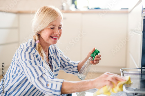 Portrait of senior woman cleaning oven in kitchen indoors at home.