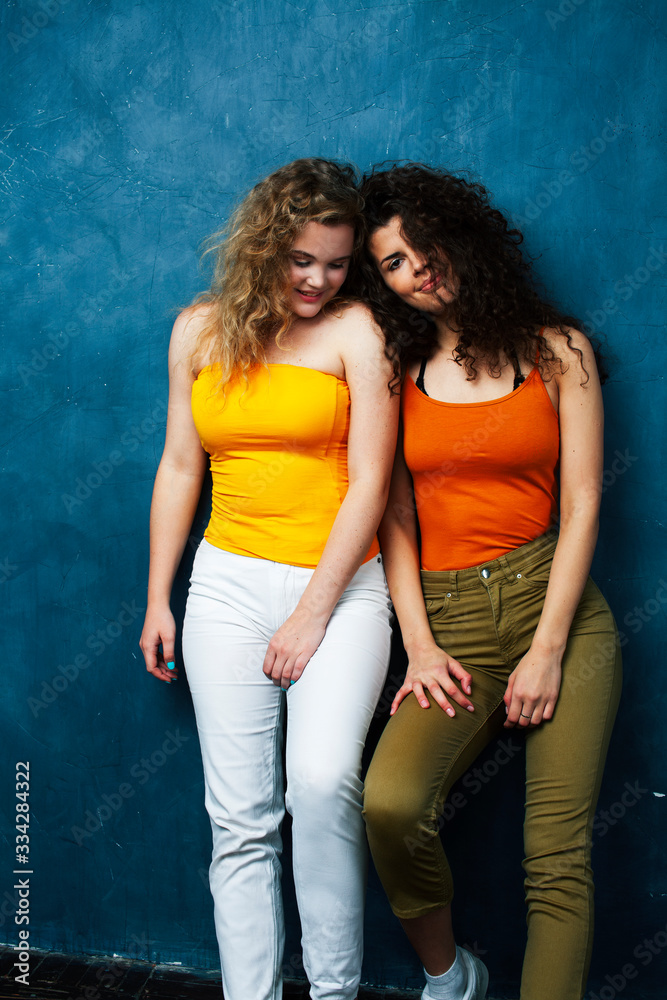 young pretty teenage girls friends with blond and brunette curly hair posing cheerful on blue background, lifestyle people concept young pretty teenage girls friends with blond and brunette curly hair posing cheerful on blue background, lifestyle people concept
