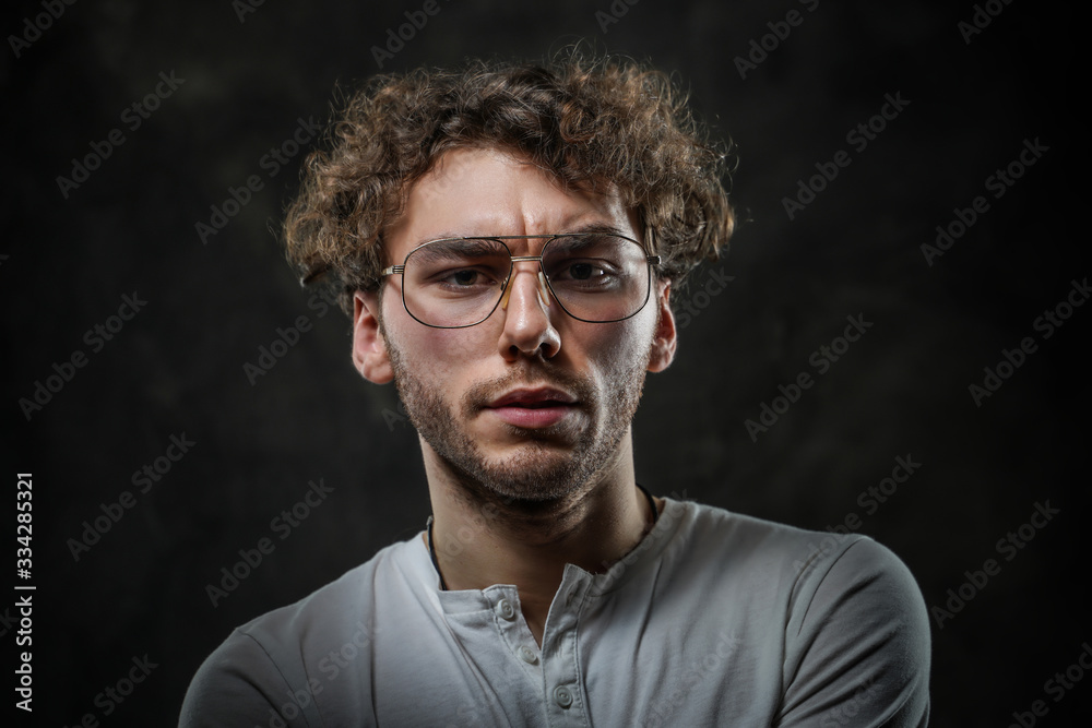 Sceptical young student posing in a dark studio on a grey background, looking focused while wearing casual white shirt and glasses. Sceptical young student posing in a dark studio on a grey background, looking focused while wearing casual white shirt and glasses.