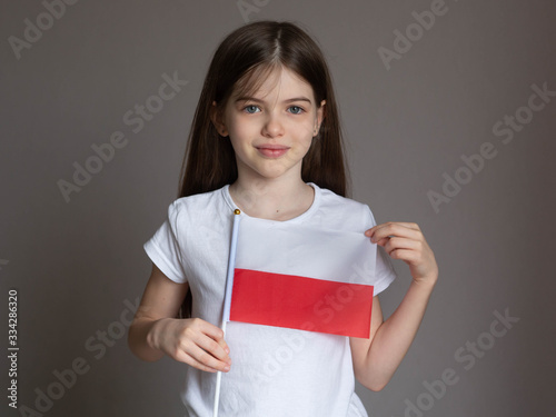 Obraz na płótnie Little / young girl with long hair in a white T-shirt holds the Polish flag. Language school concept. Learning Polish. Immigration to Poland w salonie