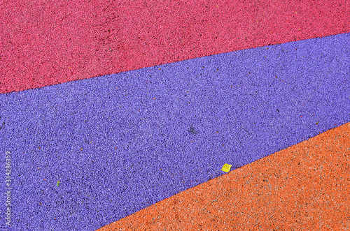 Three colors background texture - pink, violet, orange - outdoor playground floor covering with a small yellow leaf, fresh new flooring for outdoor activities