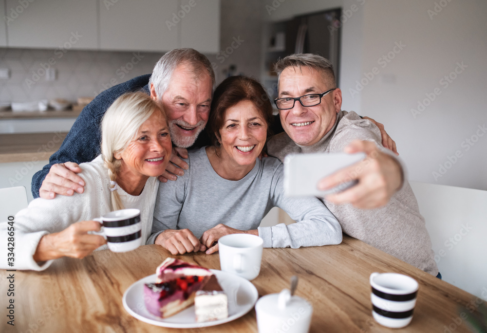 Group of senior friends at home, taking selfie with smartphone.
