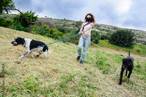 Coronavirus lockdown. Woman with face mask takes her dogs for a walk during coronavirus,running with pet. Quarantine in Mediterranean area, Italy, Spain, Cyprus. © AndrCGS