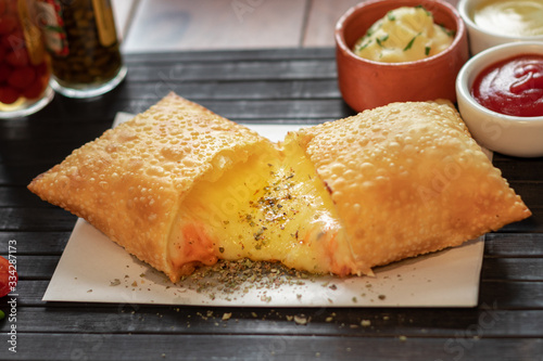 Pastel de quatro queijo com cheddar e mussarela e catupiri e gorgonzola e parmesão em uma mesa com uma esteira preta e guardanapo com fundo de molho   photo