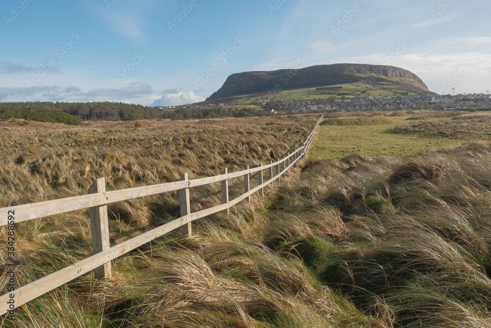 Knocknarea hill in county Sligo and Strandhill town, Ireland, Warm sunny day, clear blue sky, nobody. Wooden fence separates fields and lead to town.