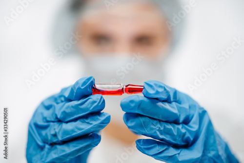 lab worker in rubber gloves holding red medicine to cure coronavirus in clinic