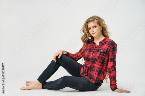 A beautiful young woman with long hair poses sitting in a shirt on a white background