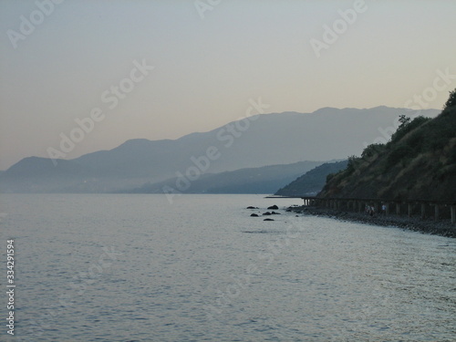 Rocky coast at sunset. In the distance, the coast mountains loomed in the mist. © SerZorin