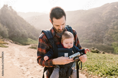 father carrying his baby daughter and taking photos on a hike on the california coast