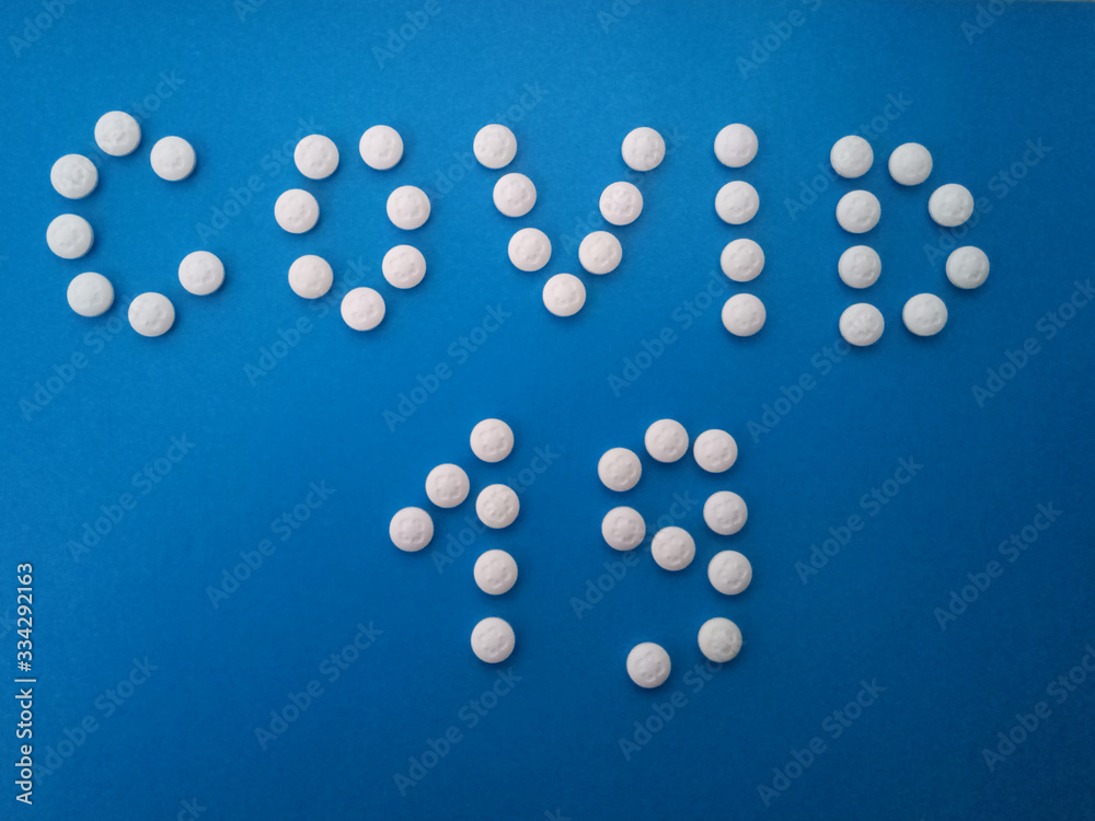 Word covid 19 made of white pills on a blue background