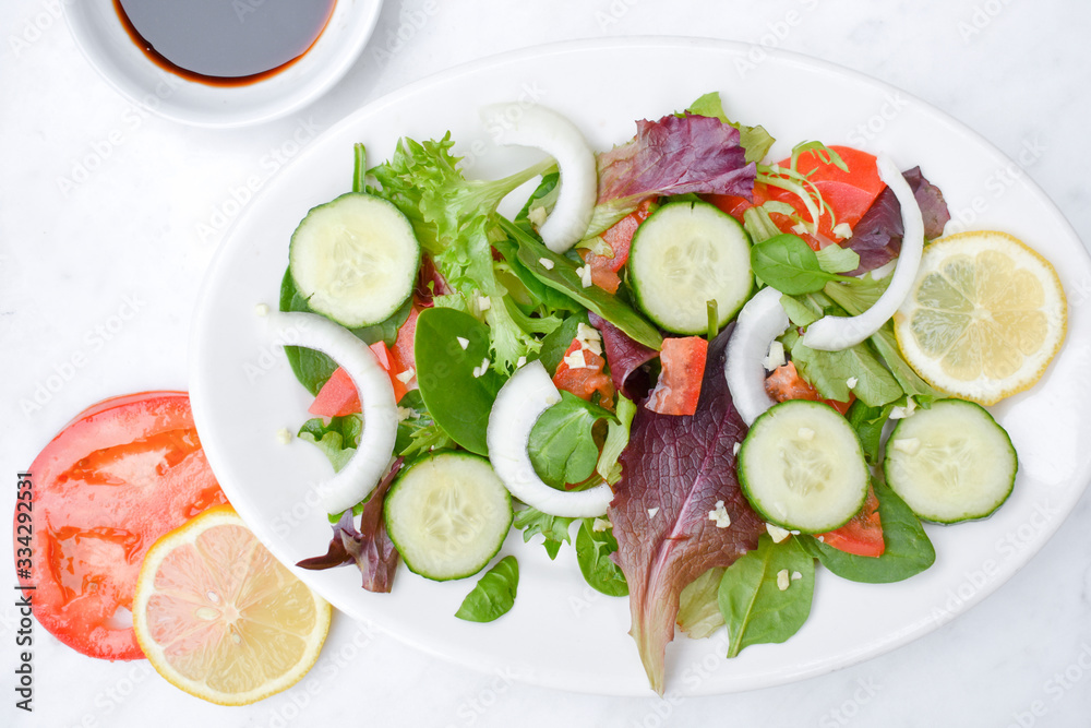 Salad with veggies and balsamic vinegar on a white plate and white table. Salad with veggies and balsamic vinegar on a white plate and white table.