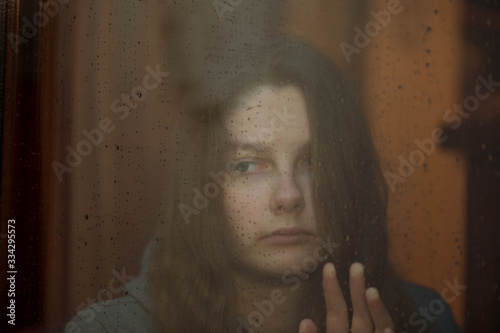 Young girl in home isolation, during quarantine for stave off preading of disease virus, near the window. COVID-19 Pandemic Coronavirus photo