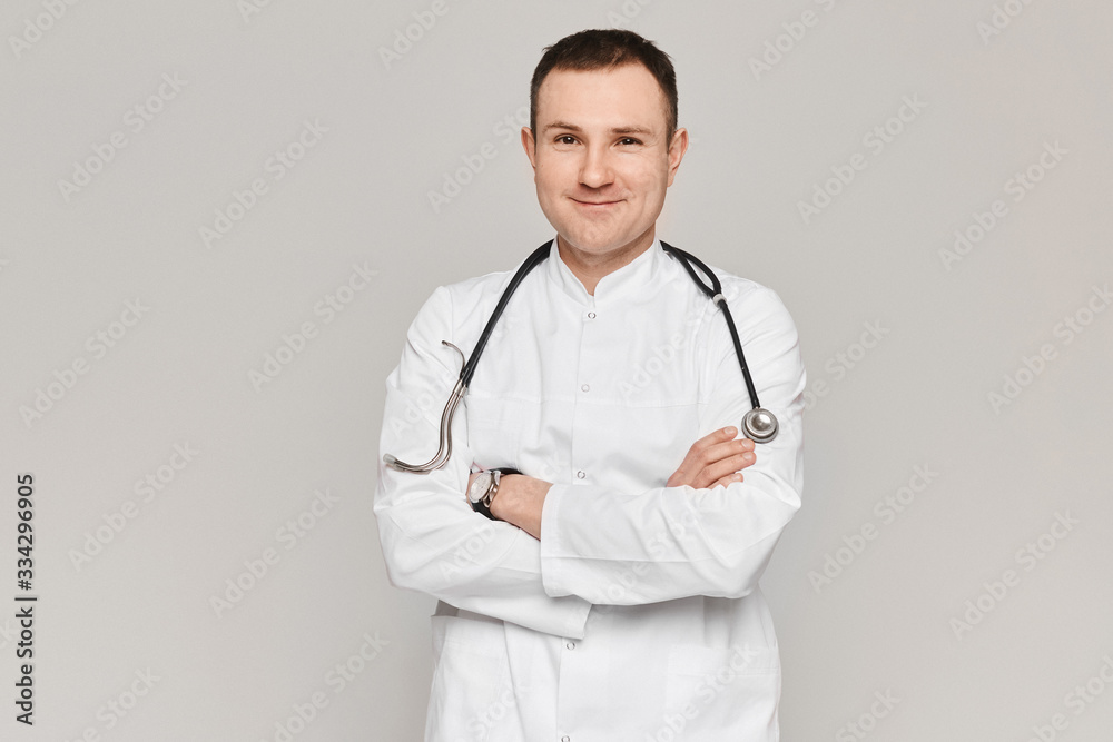 Portrait of handsome doctor posing in medical uniform with stethoscope on grey background. Concept of healthcare and professional medicine