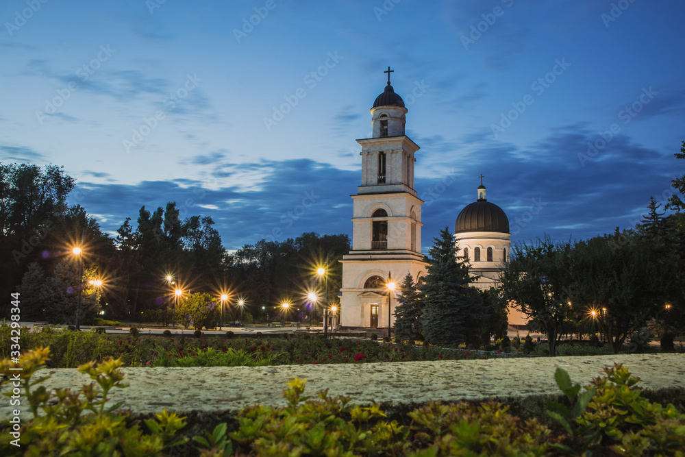 Belltower of the oldest Orthodox church in Chisinau, Moldova on a summer evening, viewed from the main plateau of cathedral, with flowers in the foreground. Photo taken at blue hour.