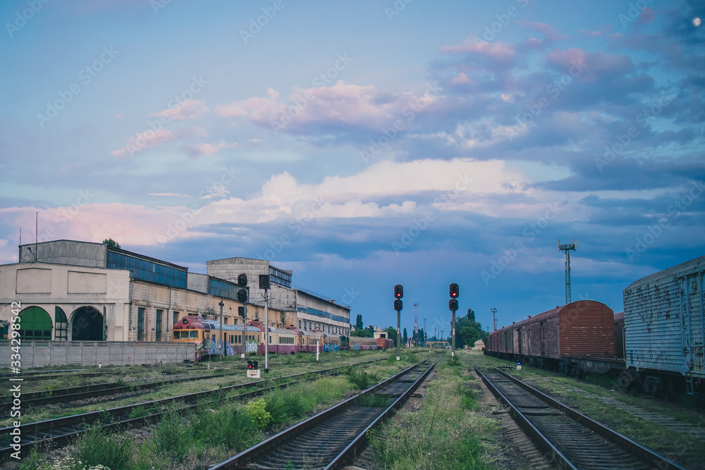 Far side of train station in Chisinau, Moldova on a summer evening. Signals ar shining red, with some old trains and wagons in the background.
