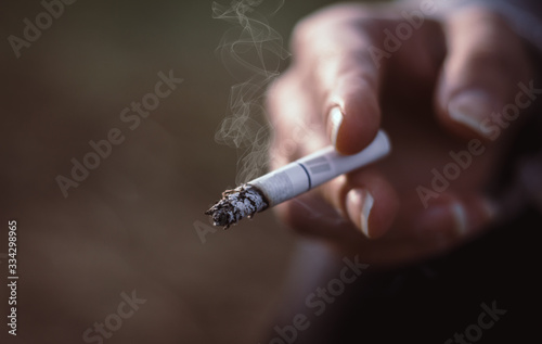 Woman holding a burning cigarette, unhealthy lifestyle concept. Bad habit, nicotine addiction, close up, copy space.