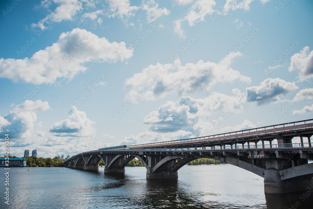Fototapeta premium Metro train in Kiev is running over the bridge over Dnieper river towards Hydropark and Dnipro district on a warm summer day in Ukraine.