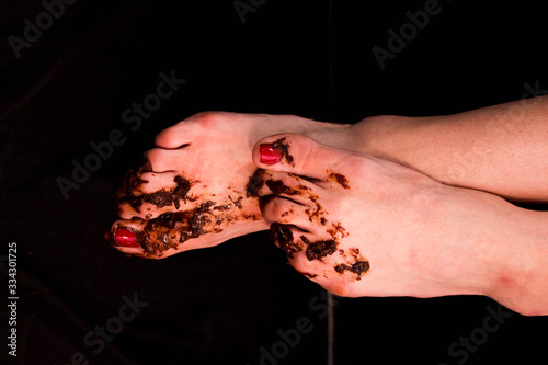 Girl's dirty bare feet stained with mud with painted red nails. On a black background