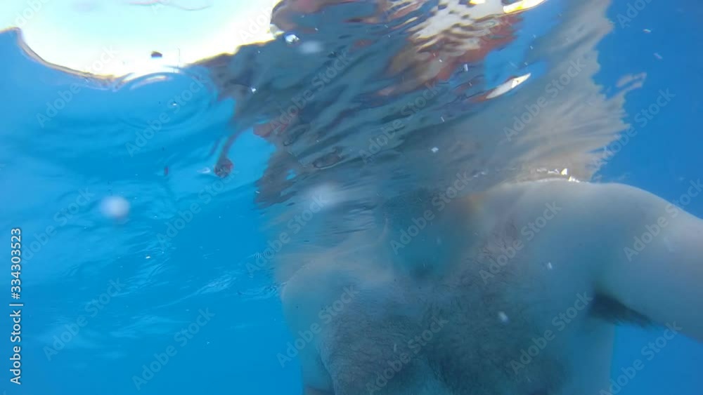 Slow motion of slightly obese man with long hair going under water and getting inside flamingo floating tube from.