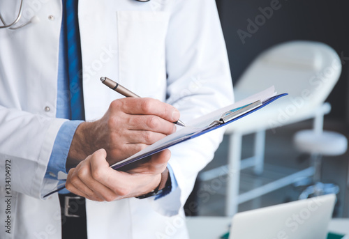 Senior male doctor with clipboard in clinic, closeup