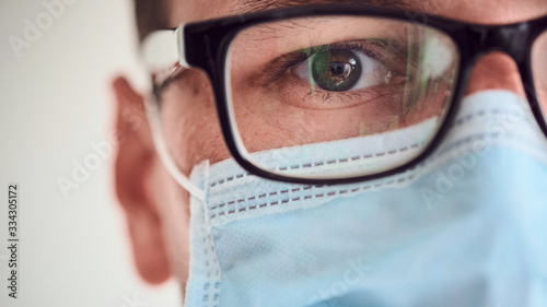 Close-up of young man face in medical mask and glasses looking at the camer photo