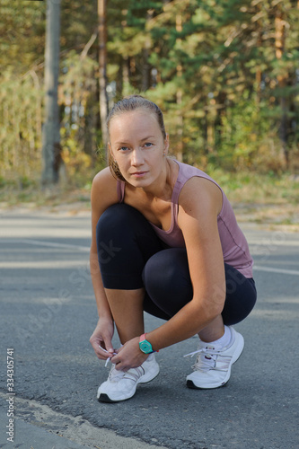 A young woman in a sportswear with a turquoise watch in her arms ties the cross outdoors