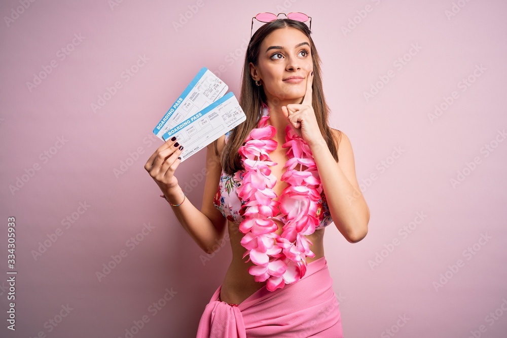 Young beautiful tourist woman on vacation wearing bikini and hawaiian lei holding boarding pass serious face thinking about question, very confused idea Young beautiful tourist woman on vacation wearing bikini and hawaiian lei holding boarding pass serious face thinking about question, very confused idea