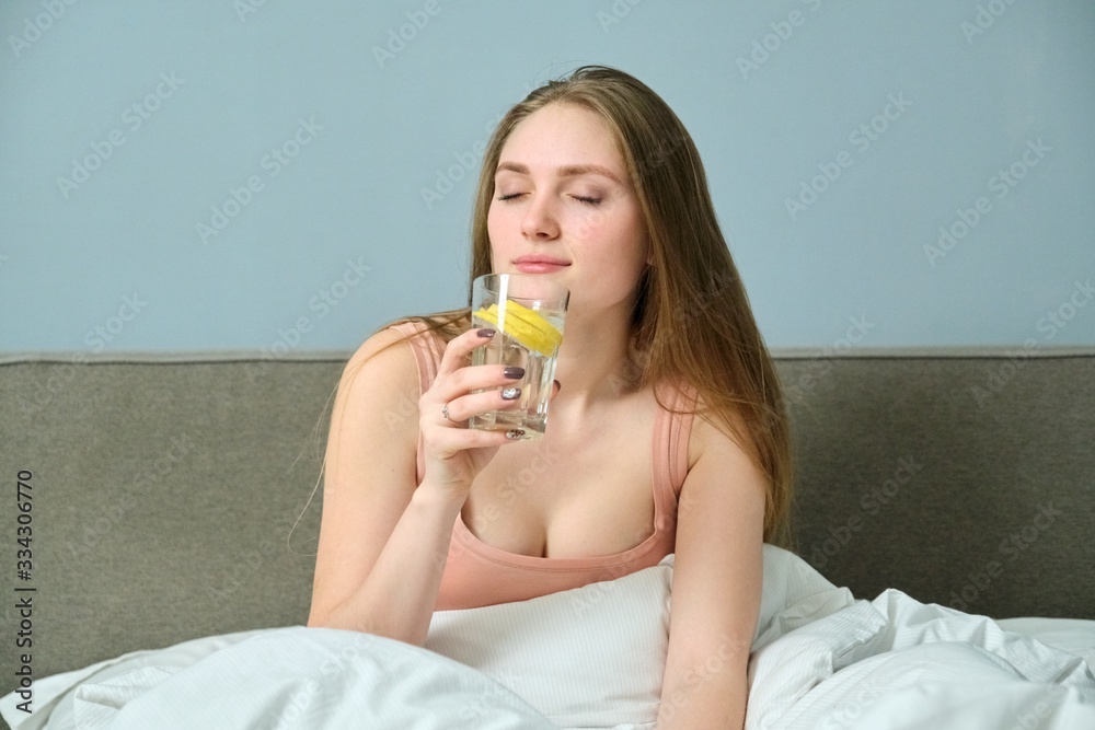 Young woman in bed with morning glass of water with lemon Young woman in bed with morning glass of water with lemon
